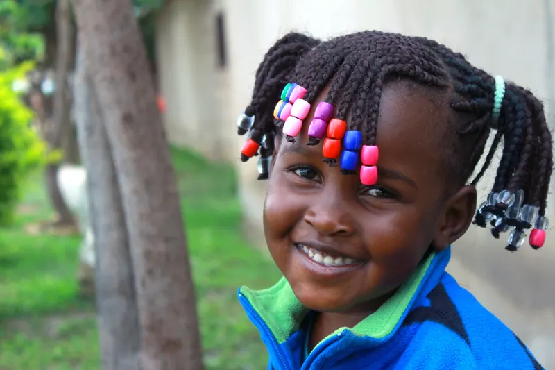 Young girl smiling outdoors with colorful beaded cornrow braids